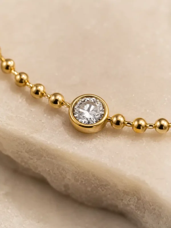 Close-up of bezel-set cubic zirconia solitaire on gold beaded bracelet