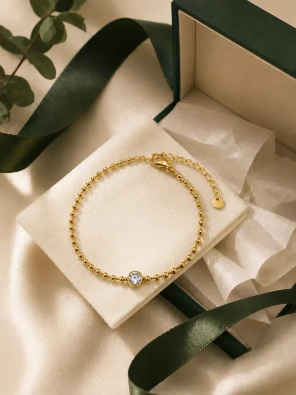Gold solitaire bead bracelet styled on cream cushion with green jewellery box