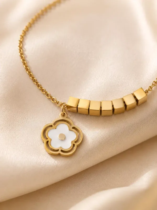 Close-up of white flower charm and polished gold cube details on Avira bracelet