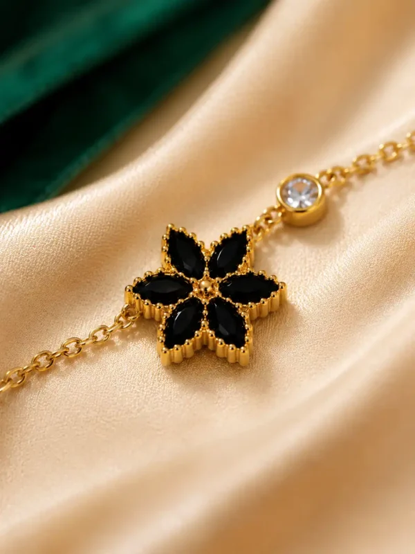 Close-up of black floral charm with gold edging and crystal accent on Noir Bloom bracelet