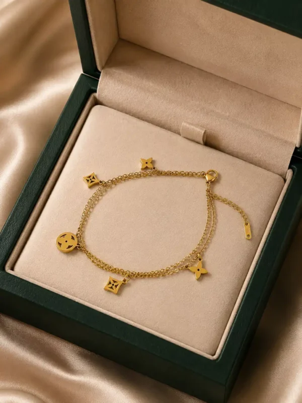Gold-toned double-layer charm bracelet displayed inside a green jewellery box with geometric motifs