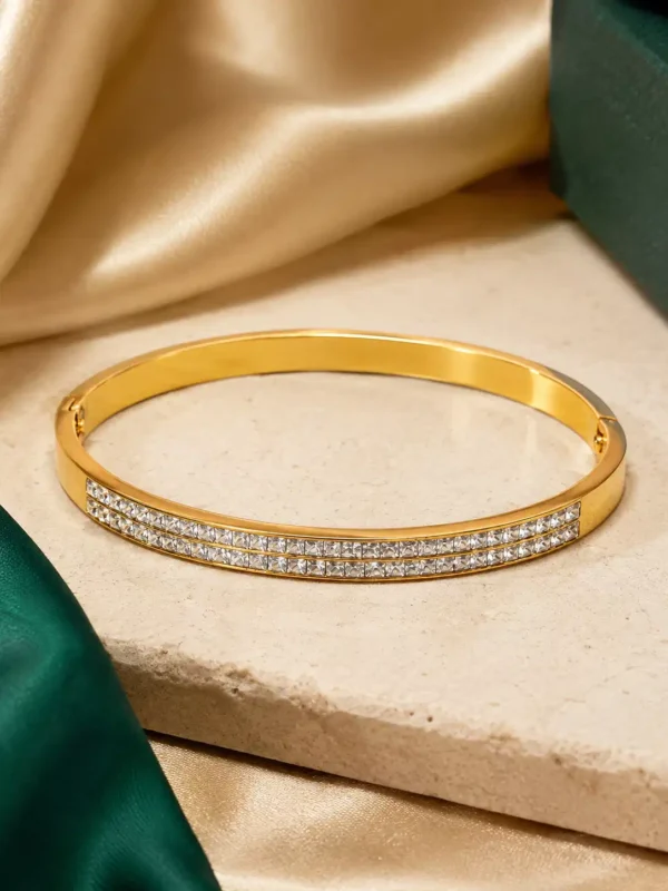 Gold-plated stainless steel bangle with two rows of clear CZ stones on a cream stone surface