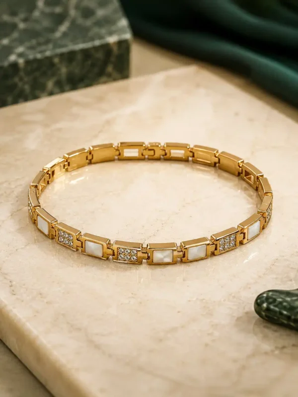 Gold geometric link bracelet with alternating white square inlays and crystal accents on a cream surface