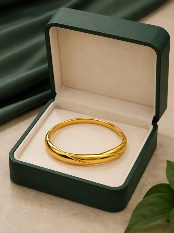 Signature Twist gold bangle displayed inside an open dark green jewellery box