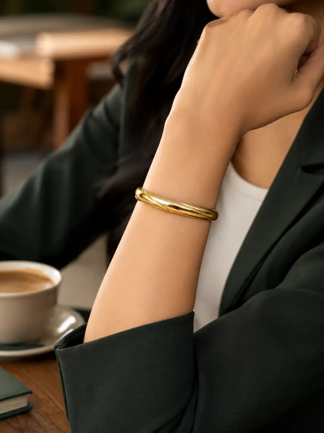 Woman wearing an anti-tarnish twisted gold bangle with a dark green blazer for office styling