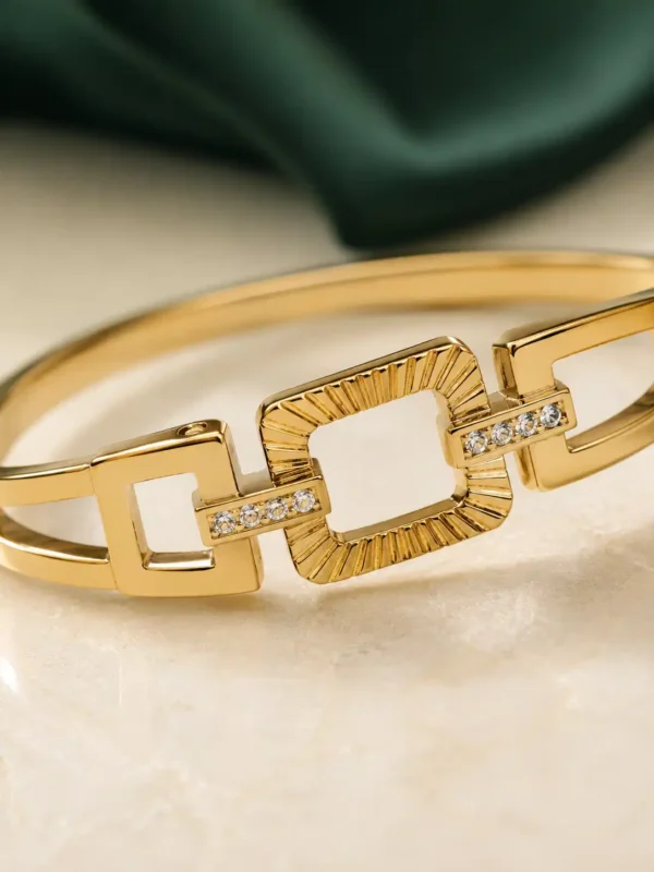 Close-up of gold geometric bangle with textured rectangular link and crystal connectors