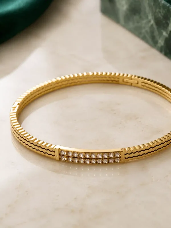 Close-up of gold bangle with double-row clear crystal pavé centre and textured band