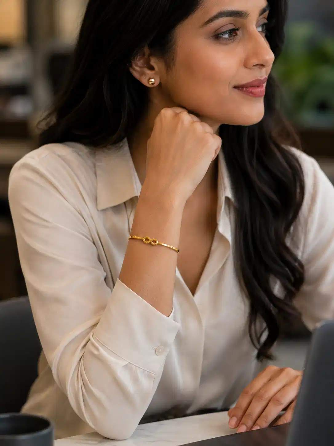 Woman wearing a minimal gold infinity bracelet with neutral office wear