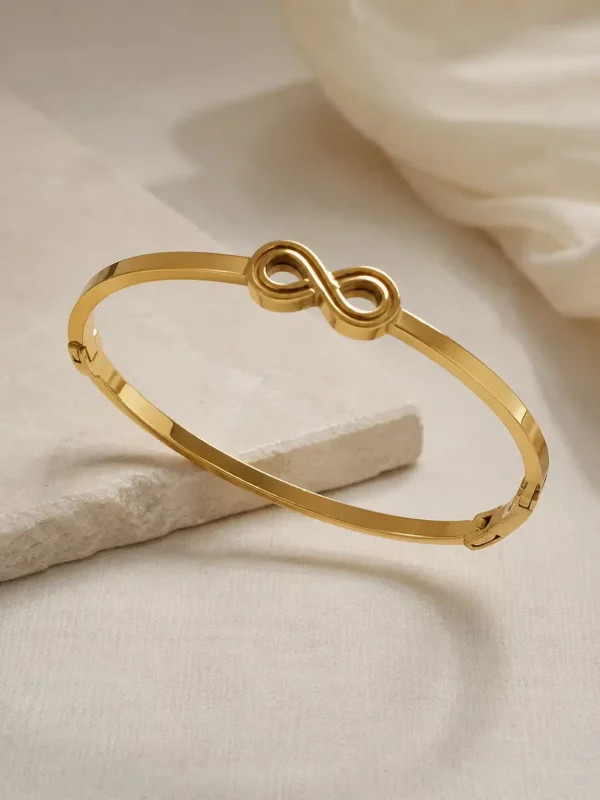 Angled view of gold stainless steel infinity bangle showing slim structured band
