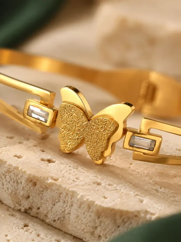 Close-up of textured gold butterfly centrepiece with rectangular crystal accents on bangle bracelet