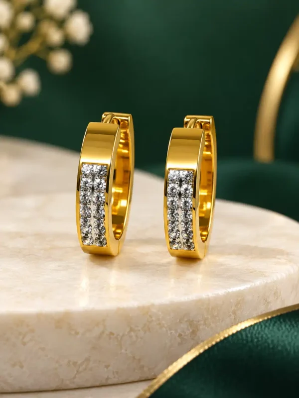 Gold anti-tarnish crystal huggie earrings displayed on cream stone surface