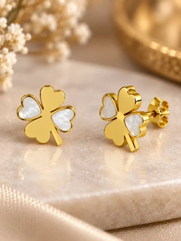 Close-up of gold four-leaf clover earrings with white mother-of-pearl heart accents