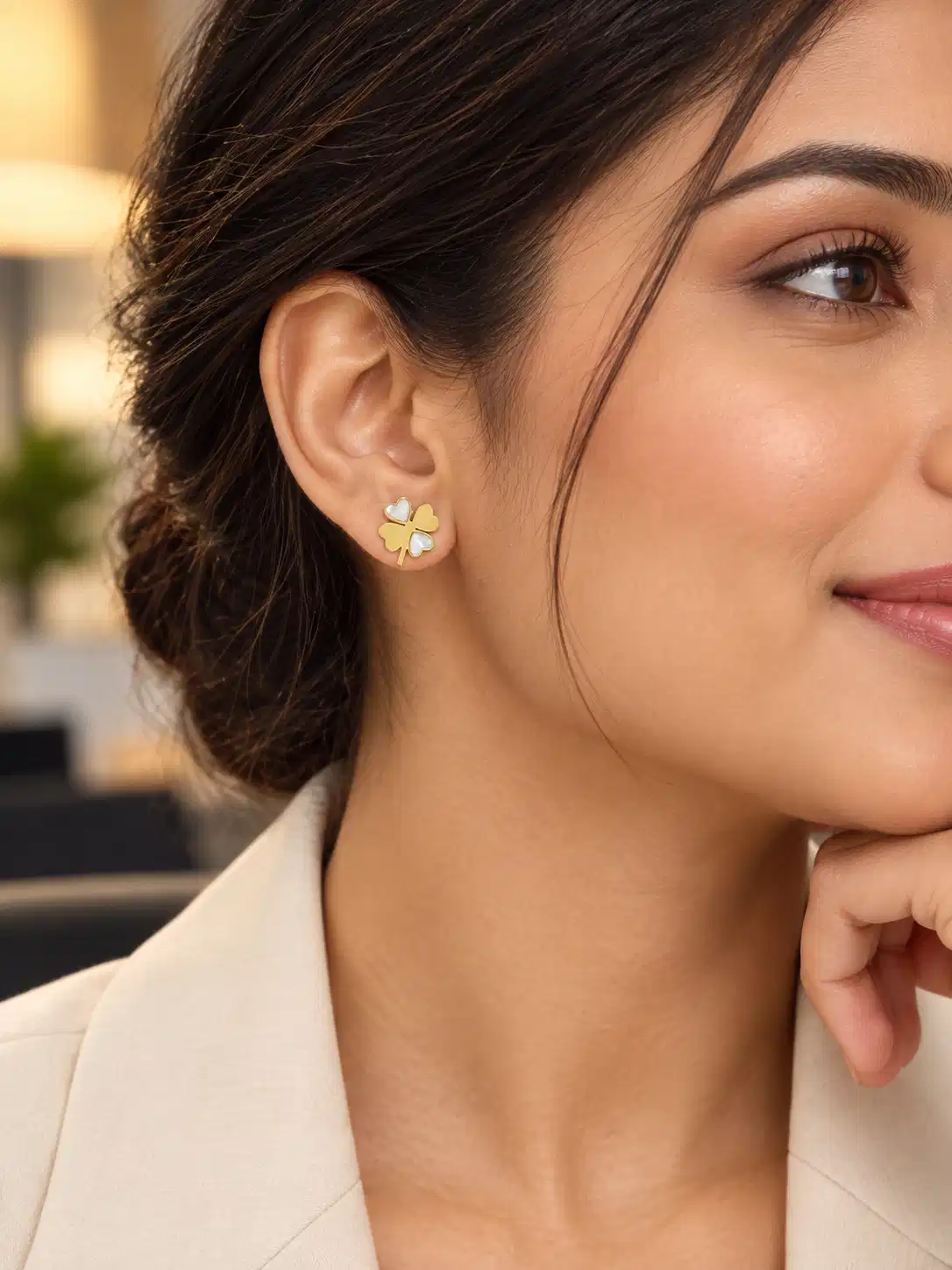 Woman wearing petite gold clover stud earrings with white mother-of-pearl details