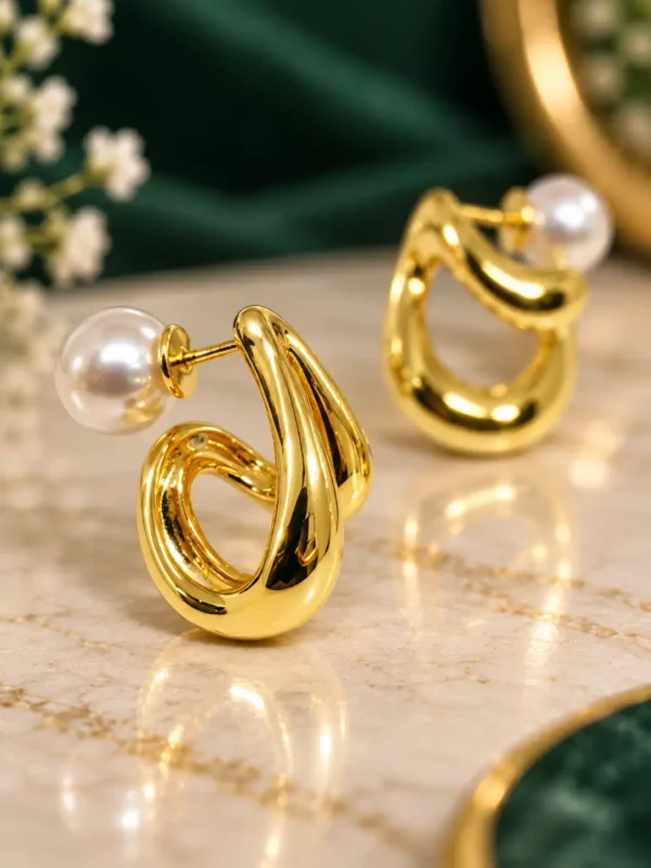 Close-up of sculpted gold swirl stud earring with white pearl accent