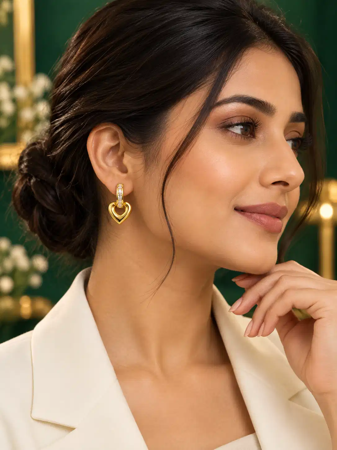 Woman wearing gold heart crystal drop earrings with an ivory blazer