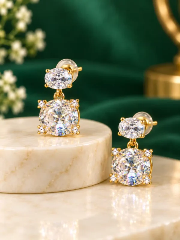 Angled pair of gold-plated double stone crystal drop earrings on a marble display