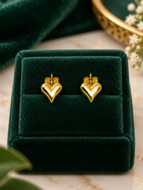Pair of gold puffy heart stud earrings displayed on dark green velvet