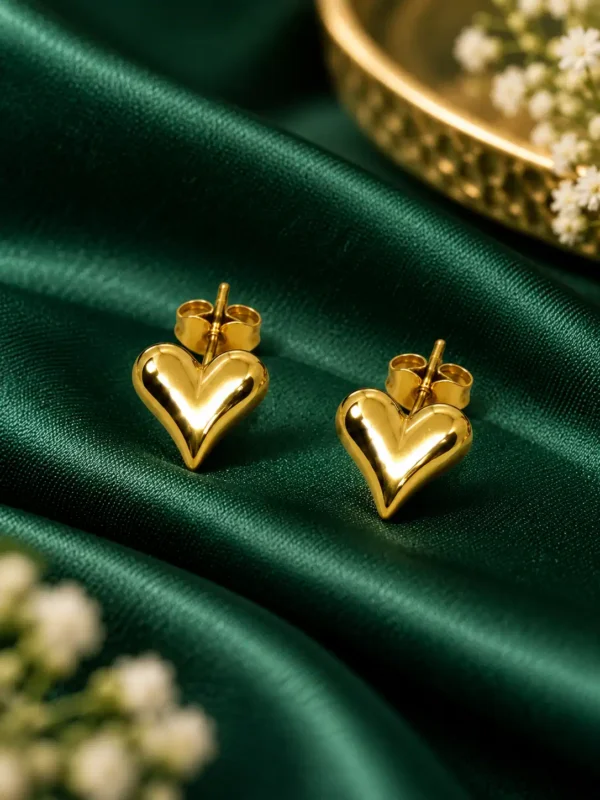 Polished gold puffy heart stud earrings styled on emerald green satin