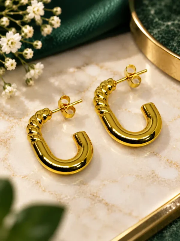 Pair of gold-plated twisted U-shape hoop earrings displayed on a marble surface