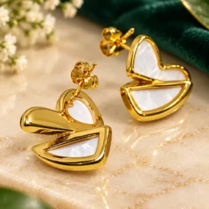 Angled close-up of gold heart stud earrings with polished finish and white mother-of-pearl inlay