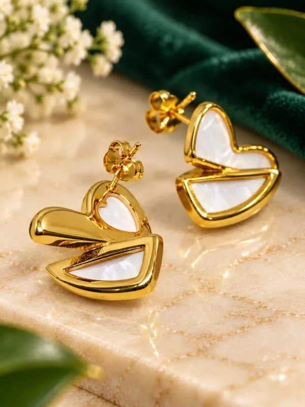 Angled close-up of gold heart stud earrings with polished finish and white mother-of-pearl inlay