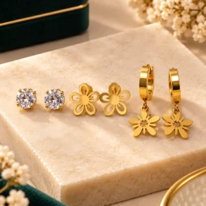 Three-pair anti-tarnish gold earring set with crystal studs, floral studs and floral drop hoops on a cream display