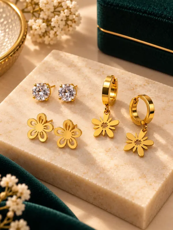 Close-up of gold-plated crystal studs, floral studs and floral drop hoop earrings on cream stone