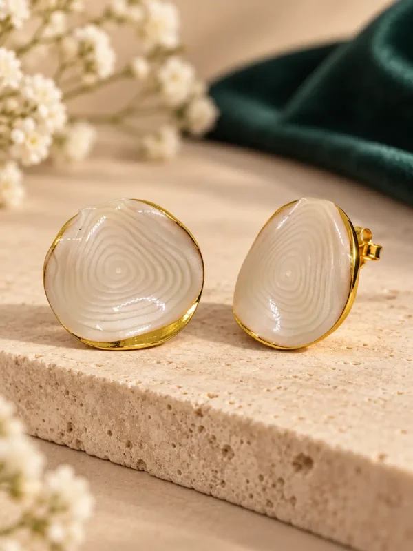 Close-up angled view of anti-tarnish ivory marble-look stud earrings with concentric ripple texture and gold-tone rim