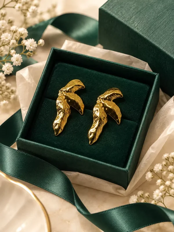 Aurelia gold wing statement stud earrings displayed in dark green jewellery box with ribbon styling