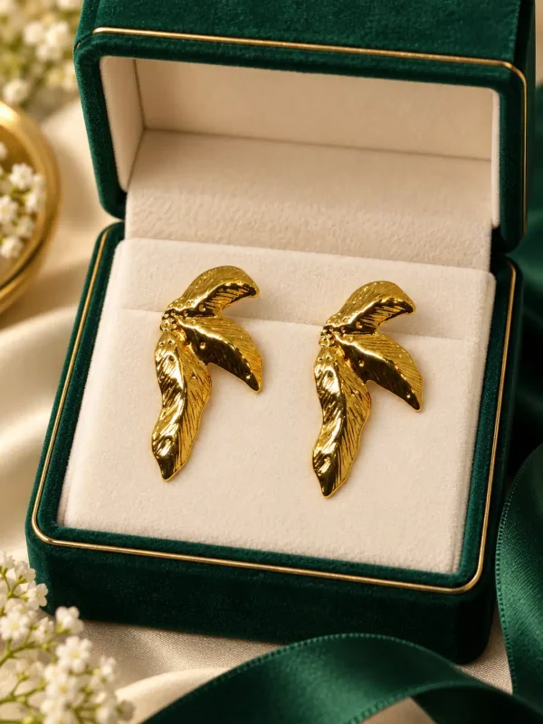 Pair of Aurelia textured gold wing stud earrings displayed in a green and cream jewellery box