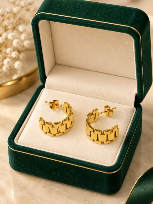 Elara gold watch-link hoop earrings displayed in dark green jewellery box