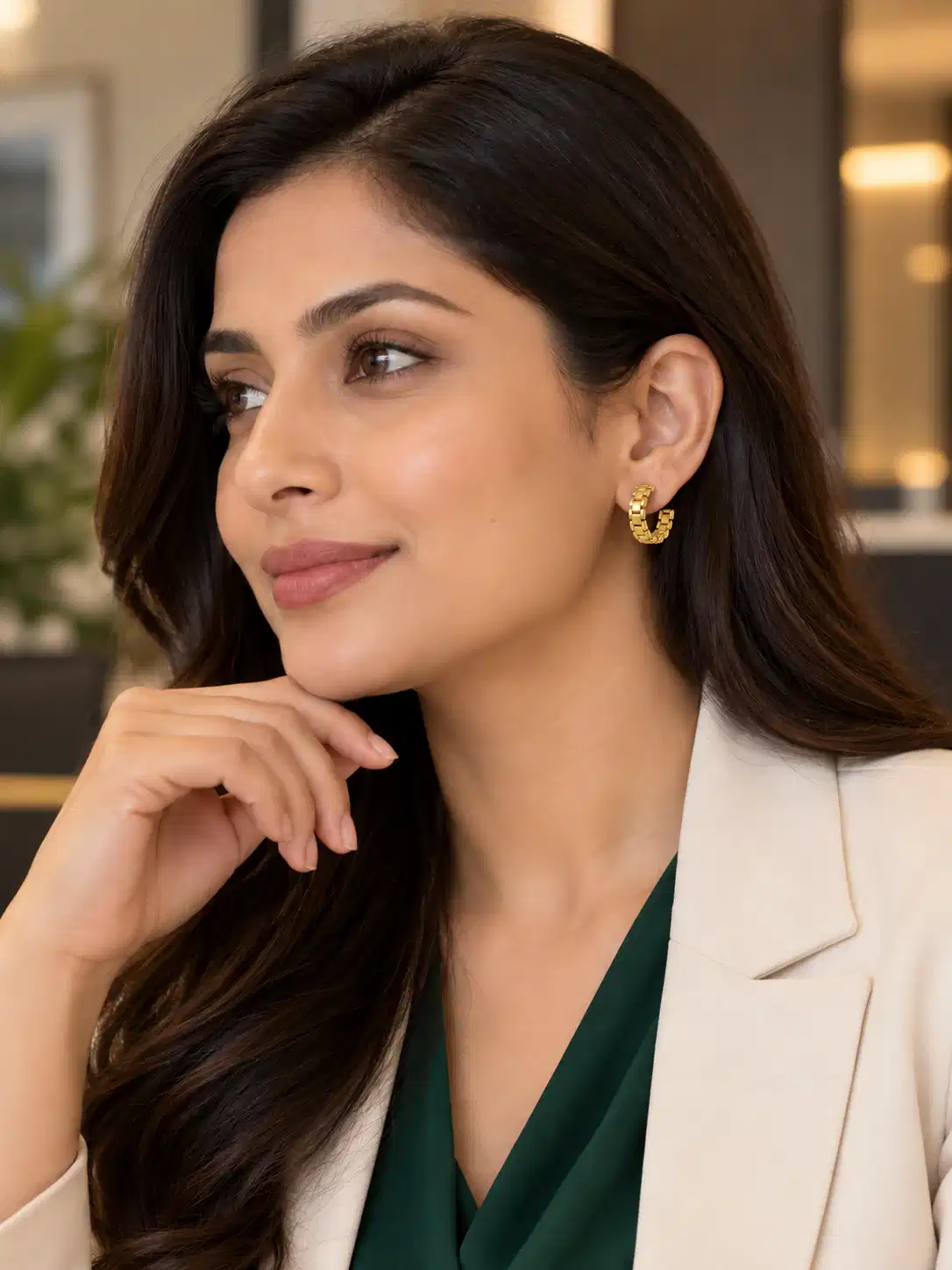 Woman wearing Elara gold watch-link hoop earrings with cream blazer and green top