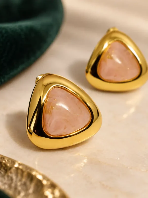 Close-up of blush pink triangular gold stud earrings with polished frame