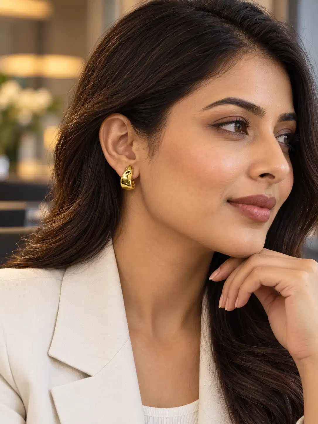 Woman wearing Amara gold sculptural half hoop earrings with a white blazer