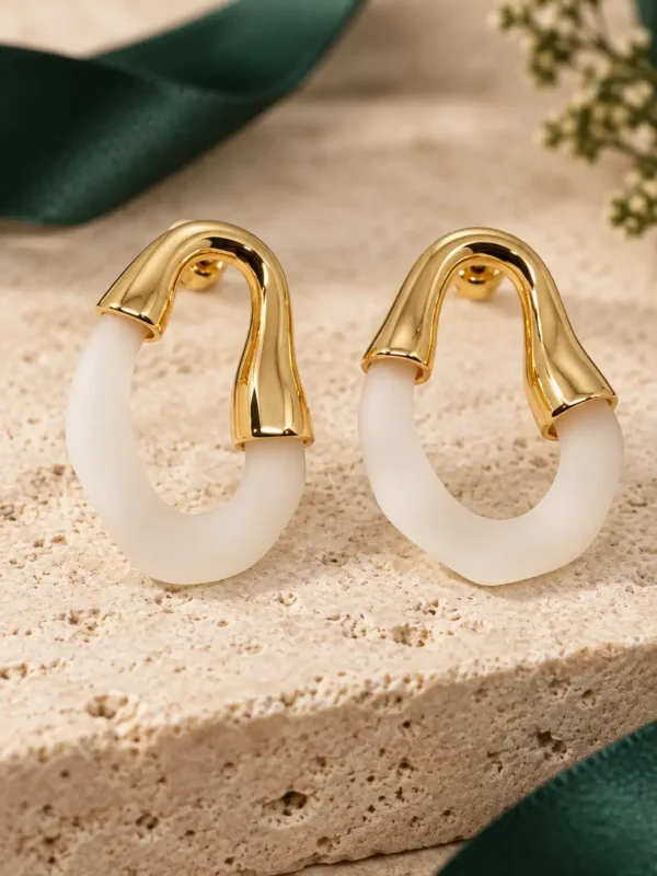 Pair of ivory and gold sculpted hoop earrings displayed on stone surface
