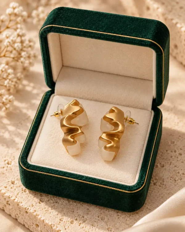 Ivory Wave gold and white sculptural earrings displayed in a green velvet jewellery box