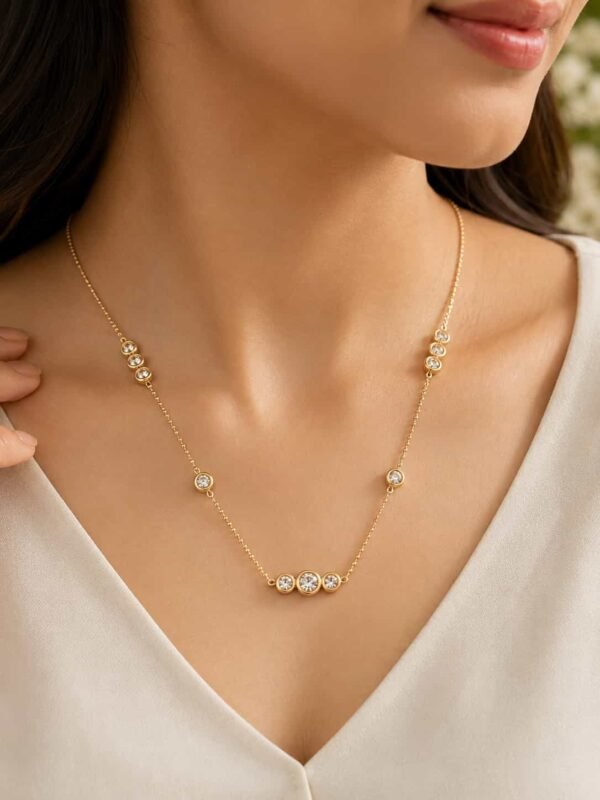 Woman wearing Aurelia gold-tone bezel station necklace with clear CZ stones and white V-neck top
