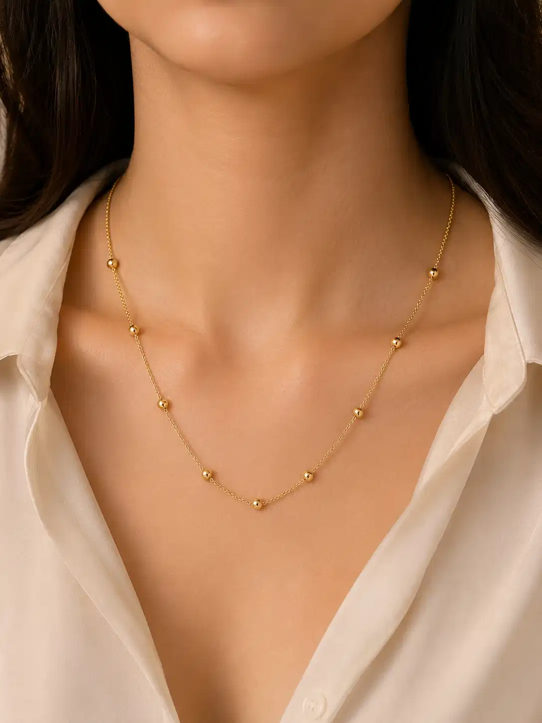 Woman wearing Solene delicate gold bead station necklace with a white open-collar shirt