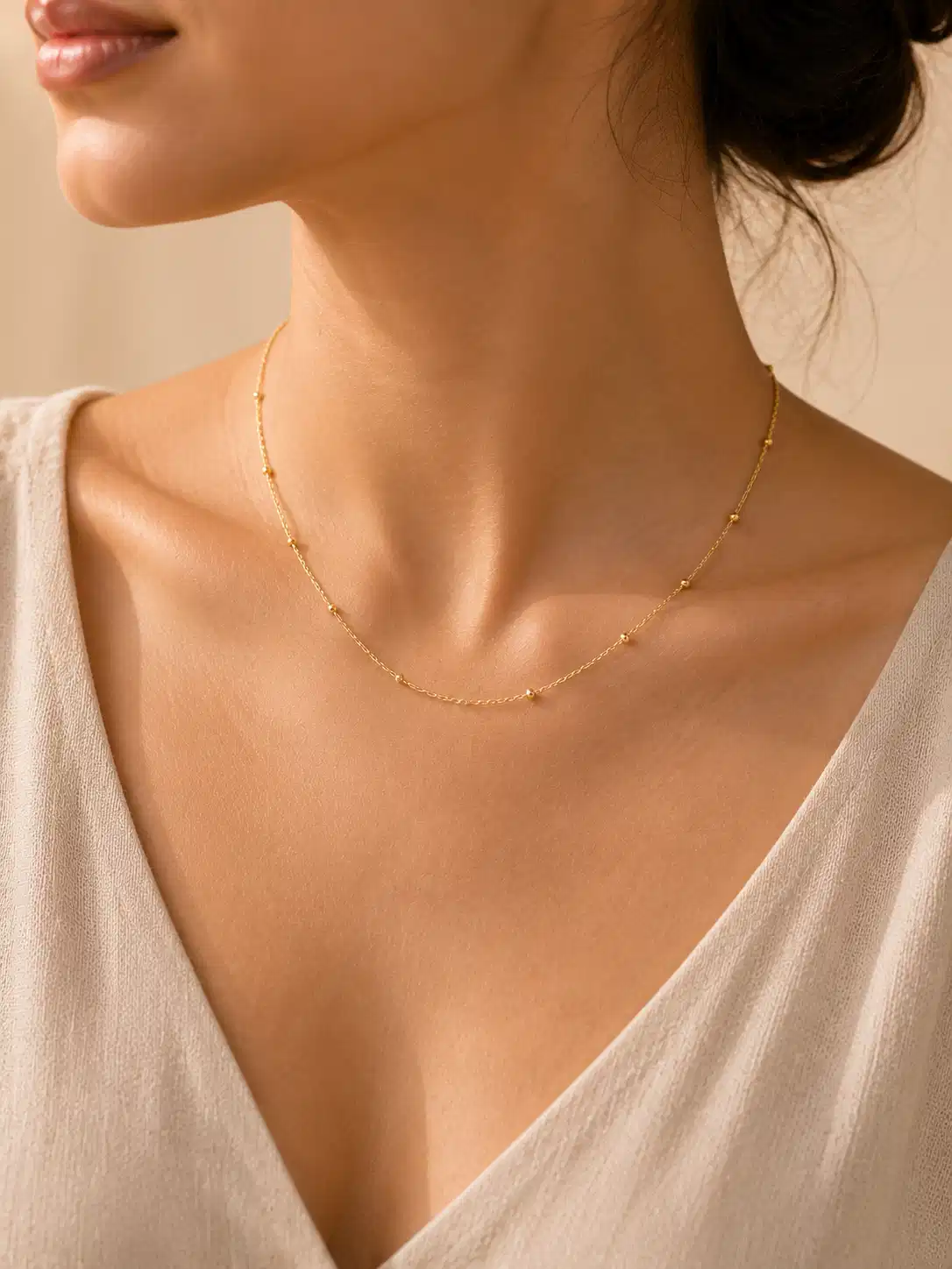 Woman wearing Evara dainty gold tiny bead necklace with cream V-neck top