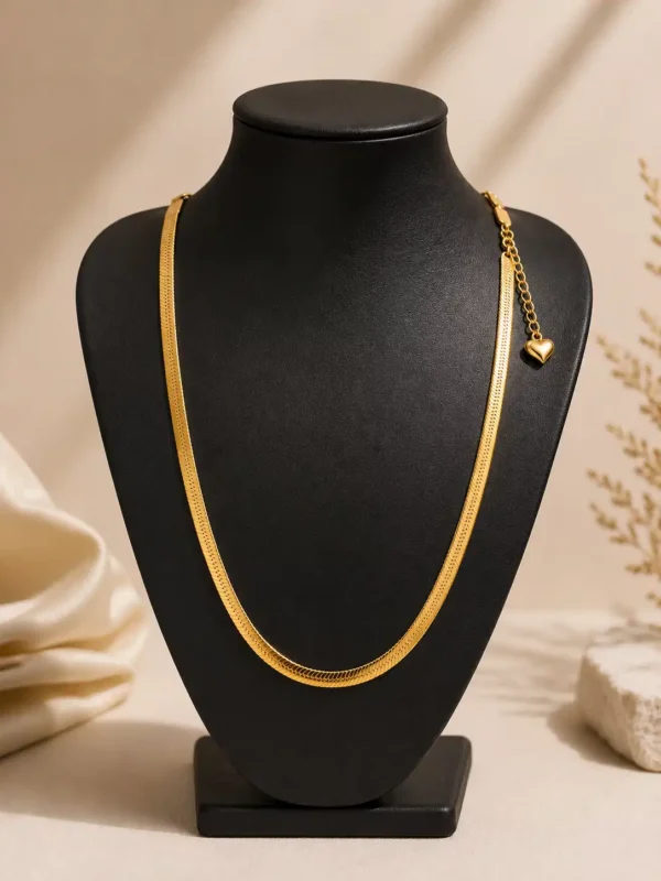Flat gold herringbone-style snake chain necklace displayed on a black jewellery bust with heart charm extension