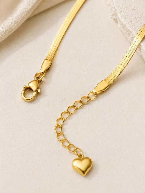 Close-up of gold flat snake chain with lobster clasp, adjustable extension links, tapered end caps and heart charm