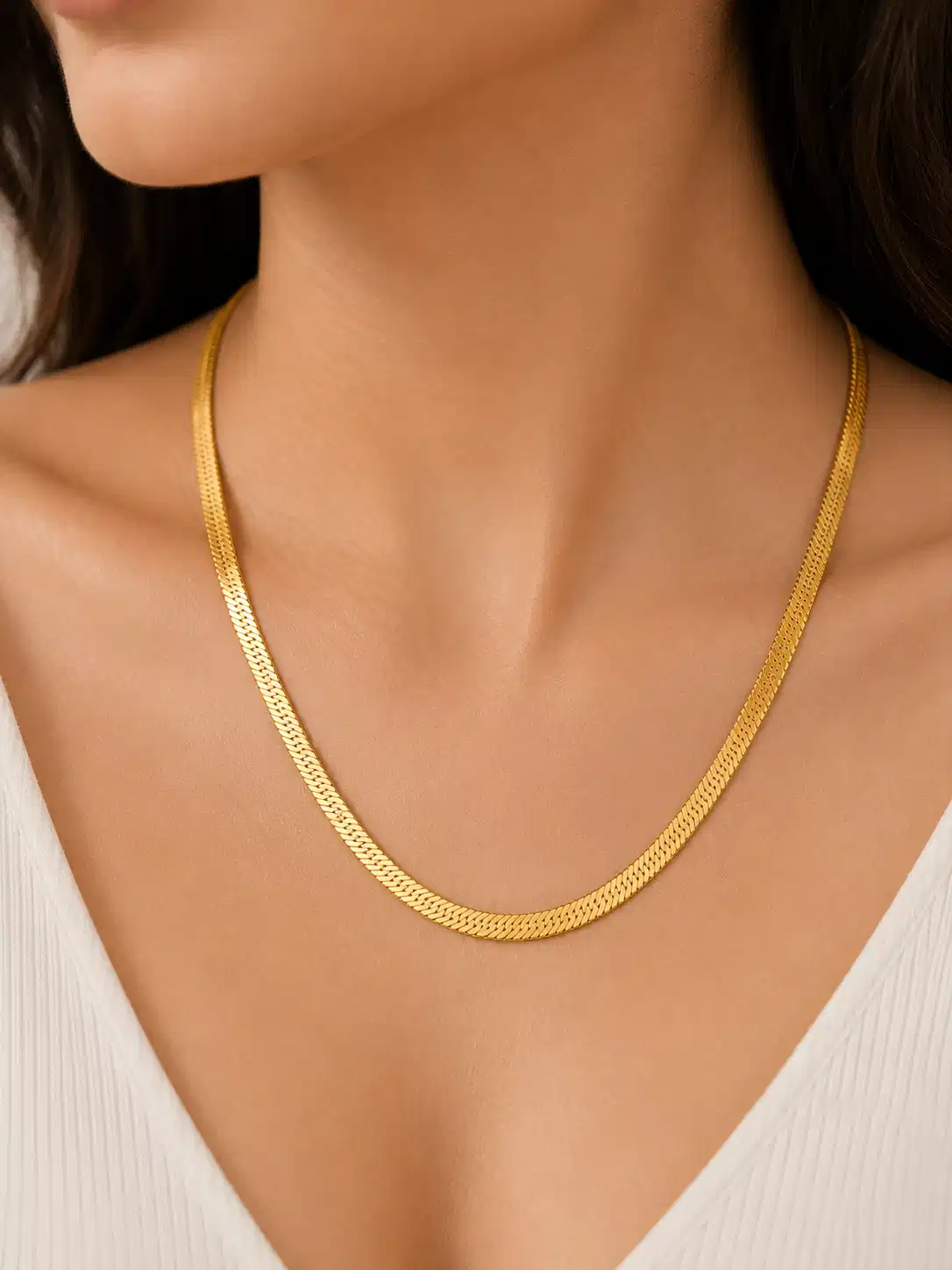 Woman wearing a polished gold-tone flat snake chain necklace with a white V-neck top