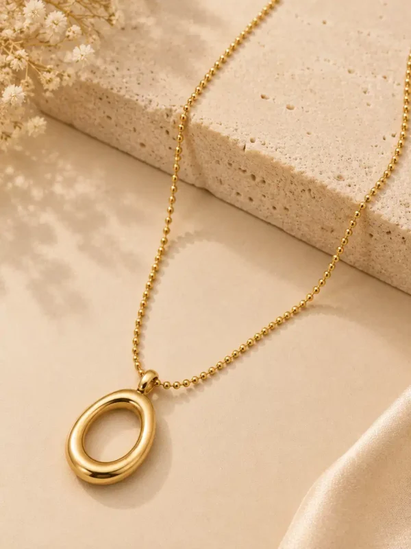 Elara Loop minimal gold oval pendant necklace styled on neutral stone