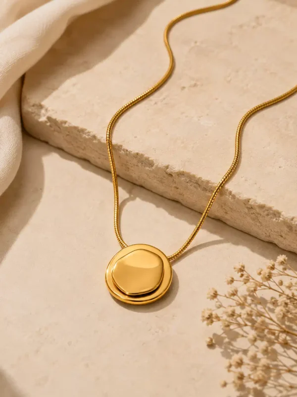 Blume Golden Orbit gold pendant necklace styled on beige stone with soft satin and dried flowers