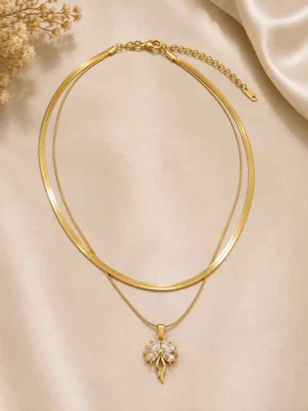 Full flat lay of Elara dual-layer gold necklace with herringbone chain, fine pendant chain and crystal flower