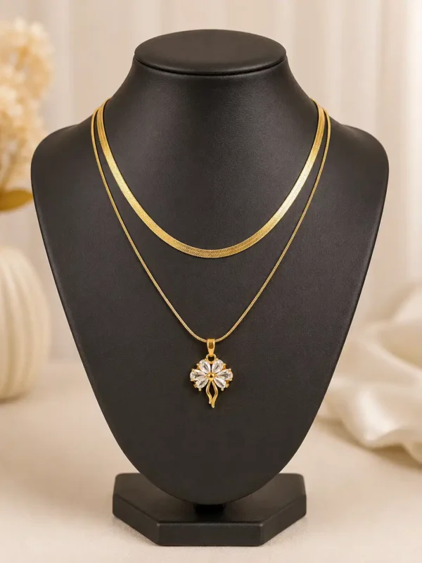 Front view of Elara gold layered necklace with flat herringbone chain and clear crystal flower pendant