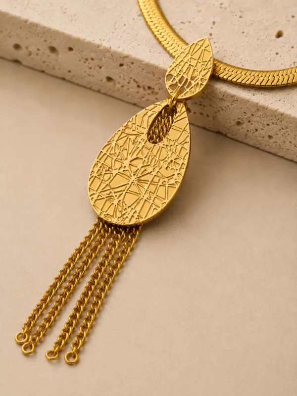 Close-up of Aurelia gold tassel necklace with geometric textured teardrop pendant and delicate hanging chain tassels