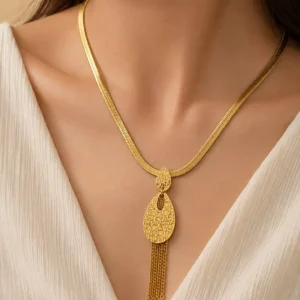 Woman wearing the Aurelia anti-tarnish gold tassel necklace with a textured teardrop pendant and white V-neck outfit