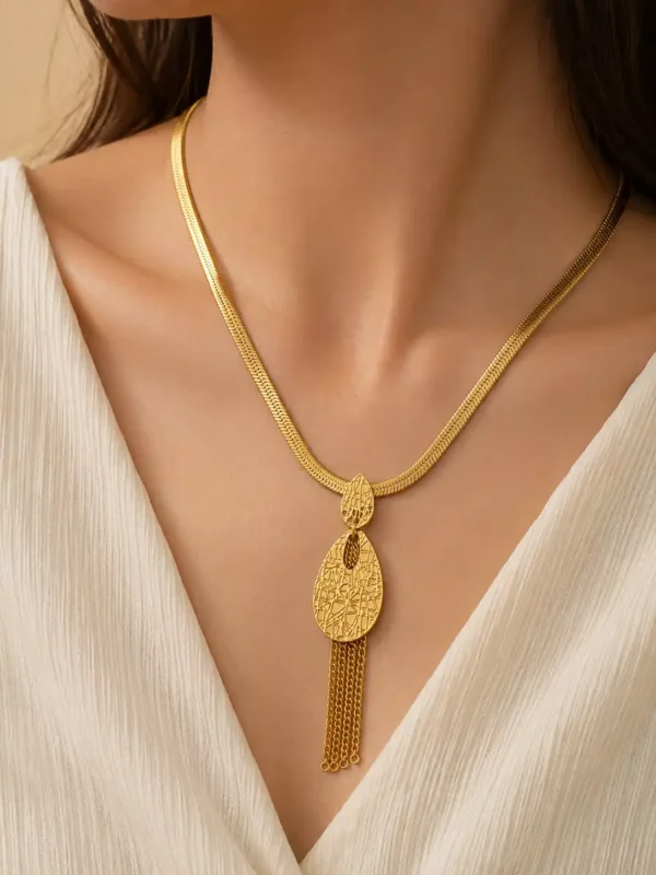 Woman wearing the Aurelia anti-tarnish gold tassel necklace with a textured teardrop pendant and white V-neck outfit