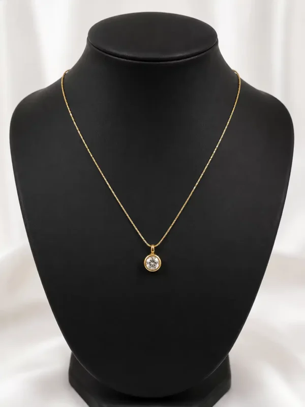 Minimal gold-tone solitaire necklace displayed on a black jewellery bust with petite round crystal pendant
